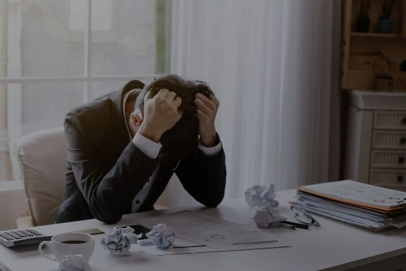 a person in a suit sitting at a desk with their head in their hands